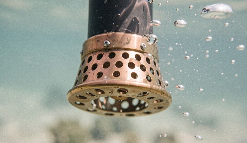 Detailaufnahme eines gelochten Messingaufsatzes am unteren Ende eines Tauchrohrs, umgeben von klarem Wasser und feinen Blasen.