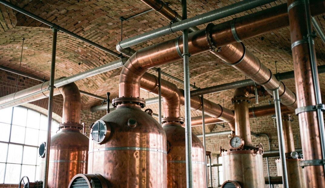 In einer alten Zuckerfabrik stehen hohe kupferne Kessel und dicke Rohrleitungen unter einem Gewölbedach aus Ziegeln.